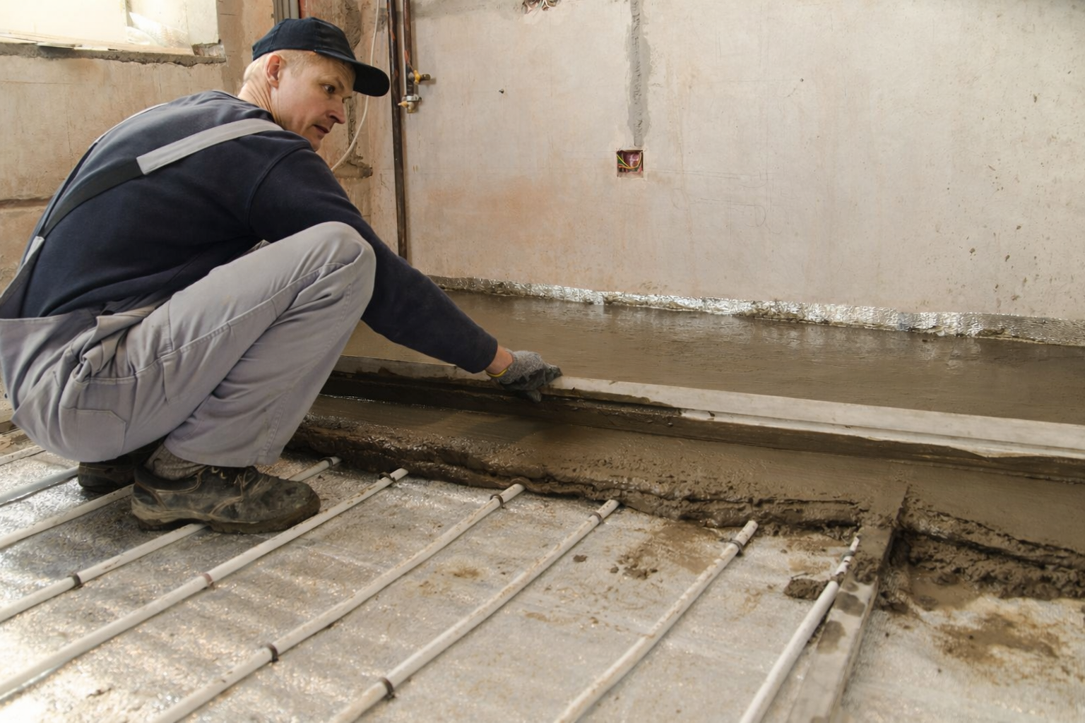 Technician applying screed over underfloor heating pipe system